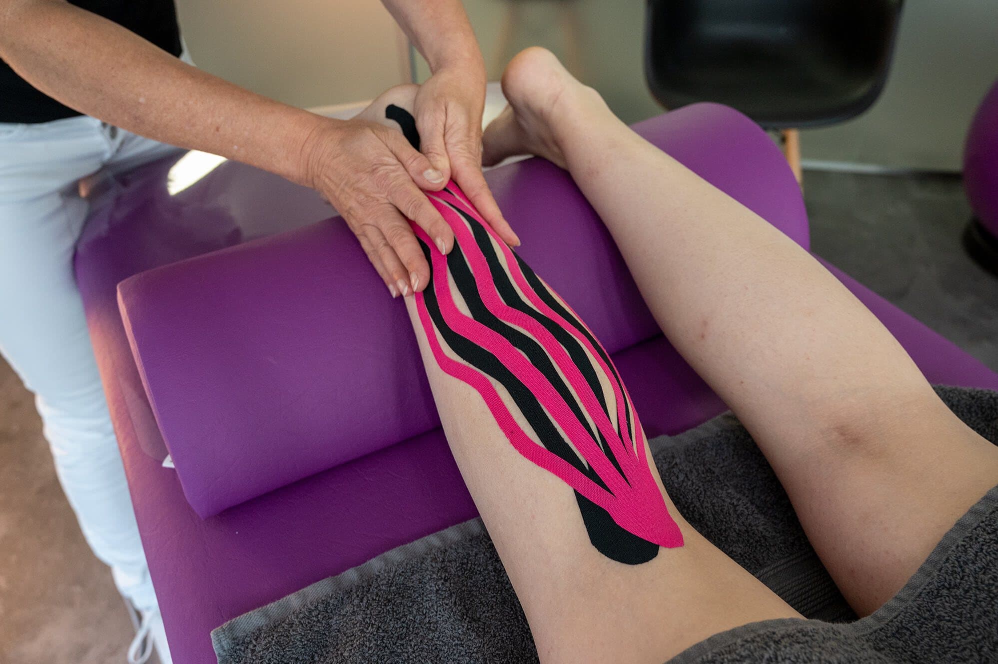 Physiotherapeutin legt ein Tape am Unterschenkel an