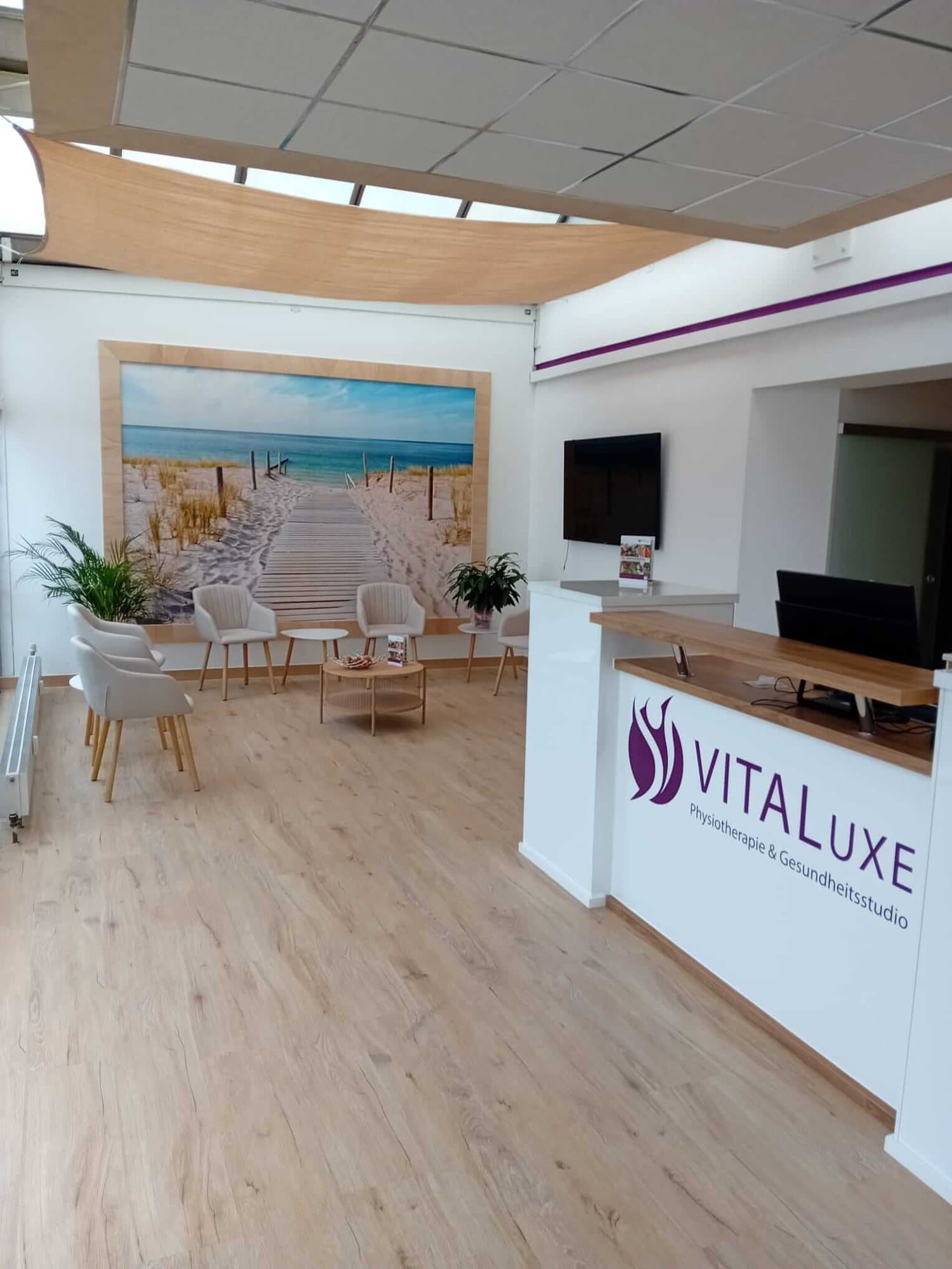 Empfang der Praxis VITALuxe Wesel: heller Wartebereich mit Holzboden vor einem großen Strandbild
